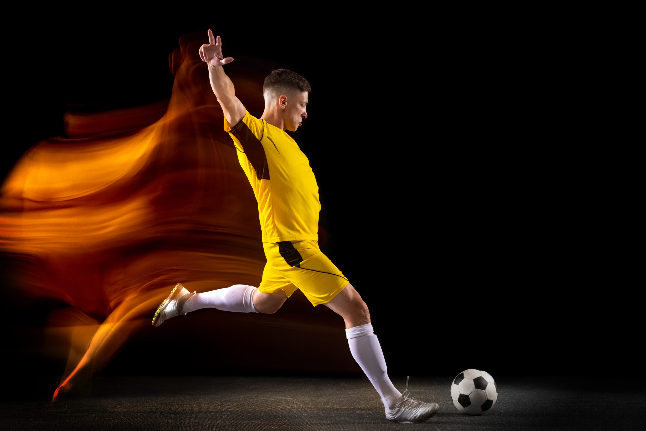young caucasian male football or soccer player kicking ball for the goal in mixed light on dark wall concept of healthy lifestyle professional sport hobby scaled