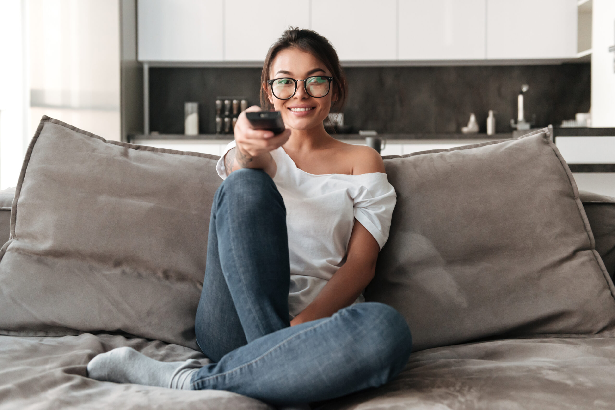 happy young woman sitting on sofa at home watch tv scaled