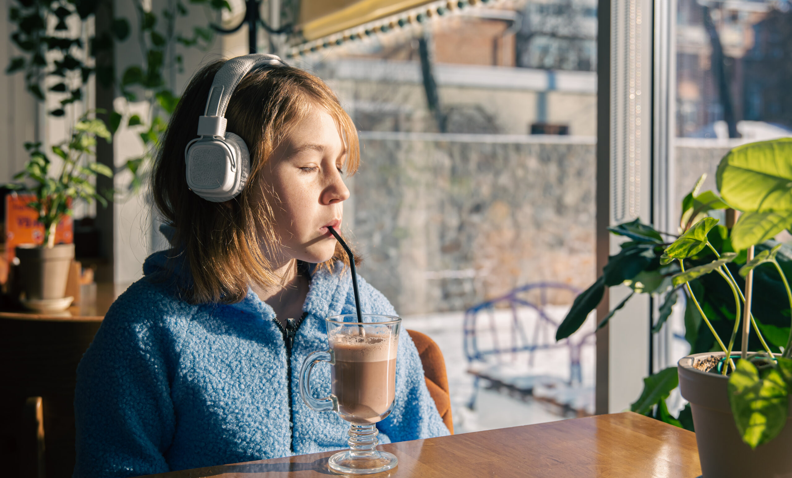 little girl listens to music in headphones and drinks cocoa with sunny morning scaled